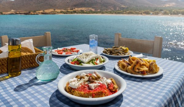 שולחן עם מנות של אוכל יווני על רקע ים והרים