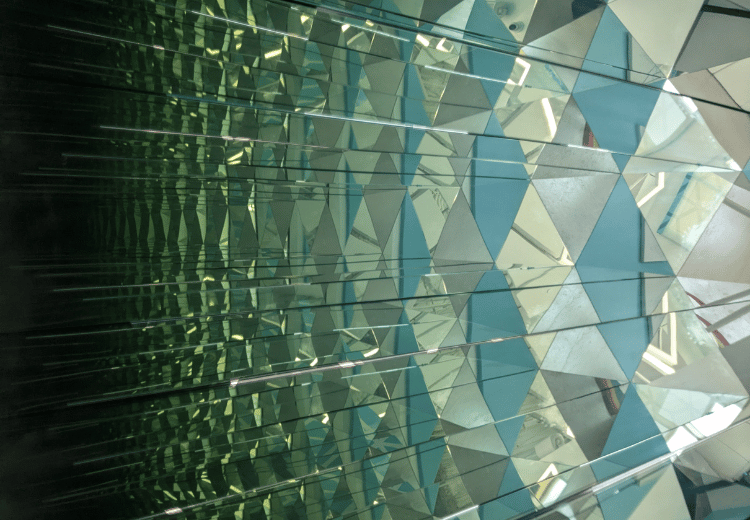 מראה של קיר עשוי ממשולשים מבריקים במוזיאון האשליות בדובאי, יוצר אפקט של עומק והשתקפויות מרובות.